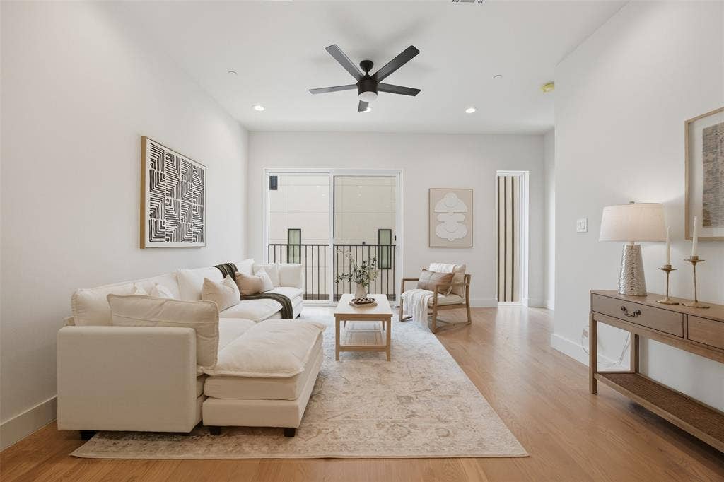 Living area featuring wood-finish flooring, recessed lighting, a matte black ceiling fan, and sliding glass doors with access to a balcony with metal railings