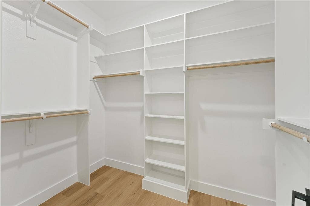 Custom walk-in closet featuring white built-in shelving, wooden closet rods, and wood-finish flooring