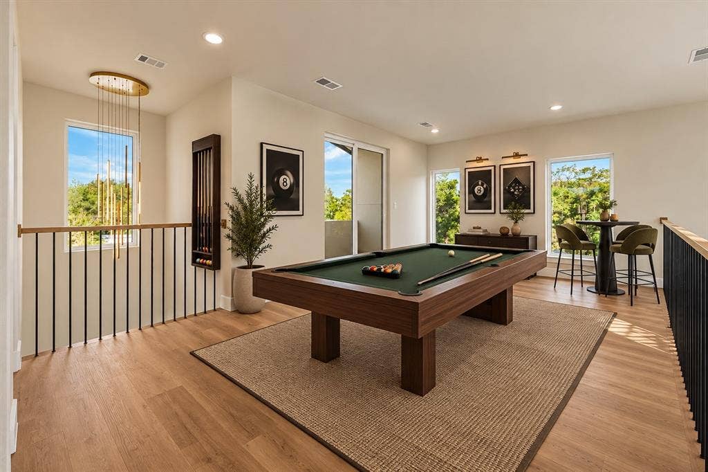 Open-concept interior featuring wood-finish flooring, recessed lighting, expansive windows, matte black metal railings, and a tiered brass pendant light fixture