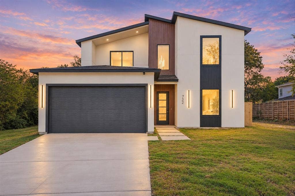 Contemporary two-story exterior featuring smooth stucco siding, vertical wood-finish accents, large rectangular windows, an attached two-car garage, and minimalist wall-mounted light fixtures