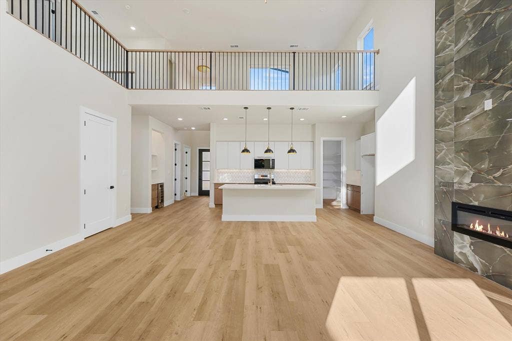 Double-height ceiling with a mezzanine overlook, full-height stone-clad linear fireplace, center island kitchen with pendant lighting, and light-toned wood-finish flooring