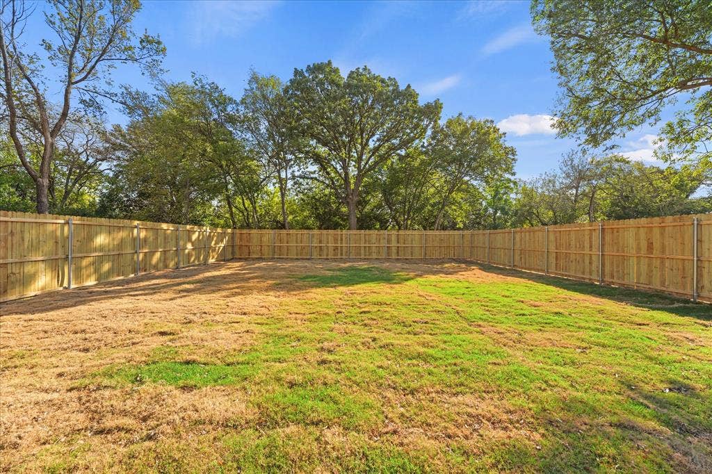 Expansive backyard featuring a wood-paneled perimeter fence, natural sod, and mature canopy trees