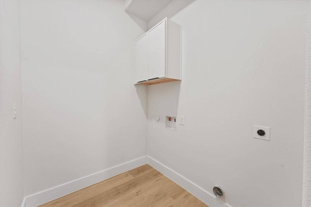 Utility area featuring wood-finish flooring, white wall-mounted cabinetry, and dedicated washer and dryer hookups