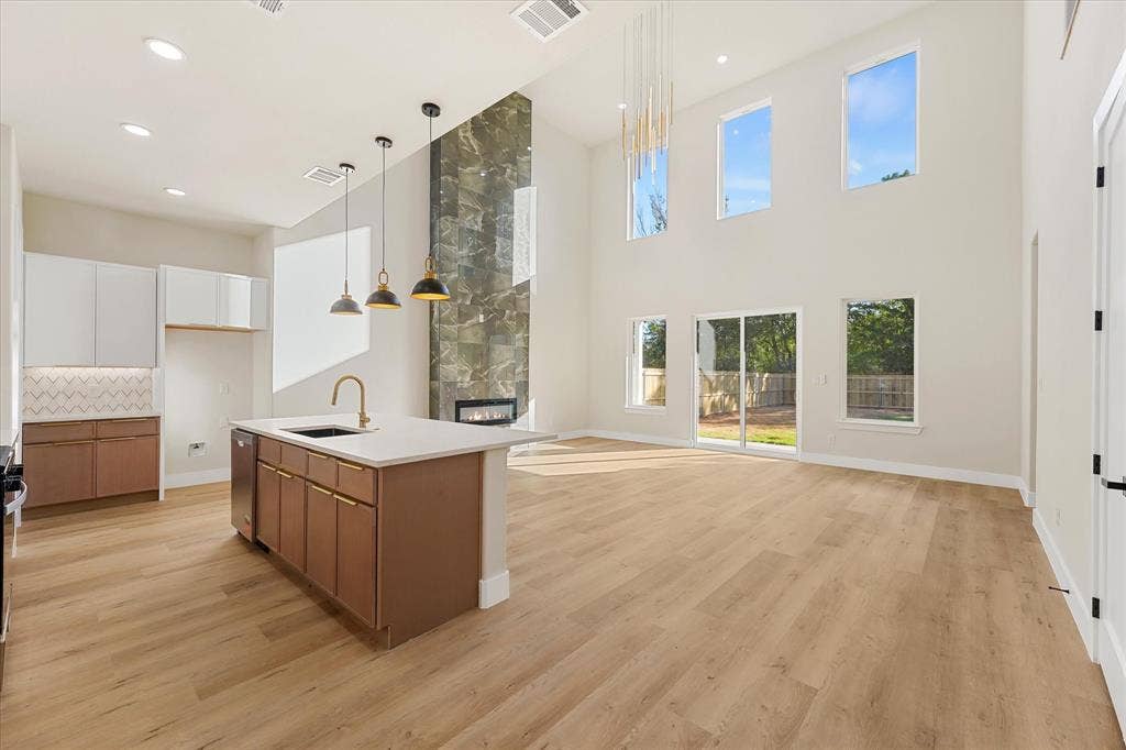 Kitchen featuring two-tone cabinetry, stone-finish countertops, herringbone-patterned tile backsplash, wood-finish flooring, and pendant lighting
