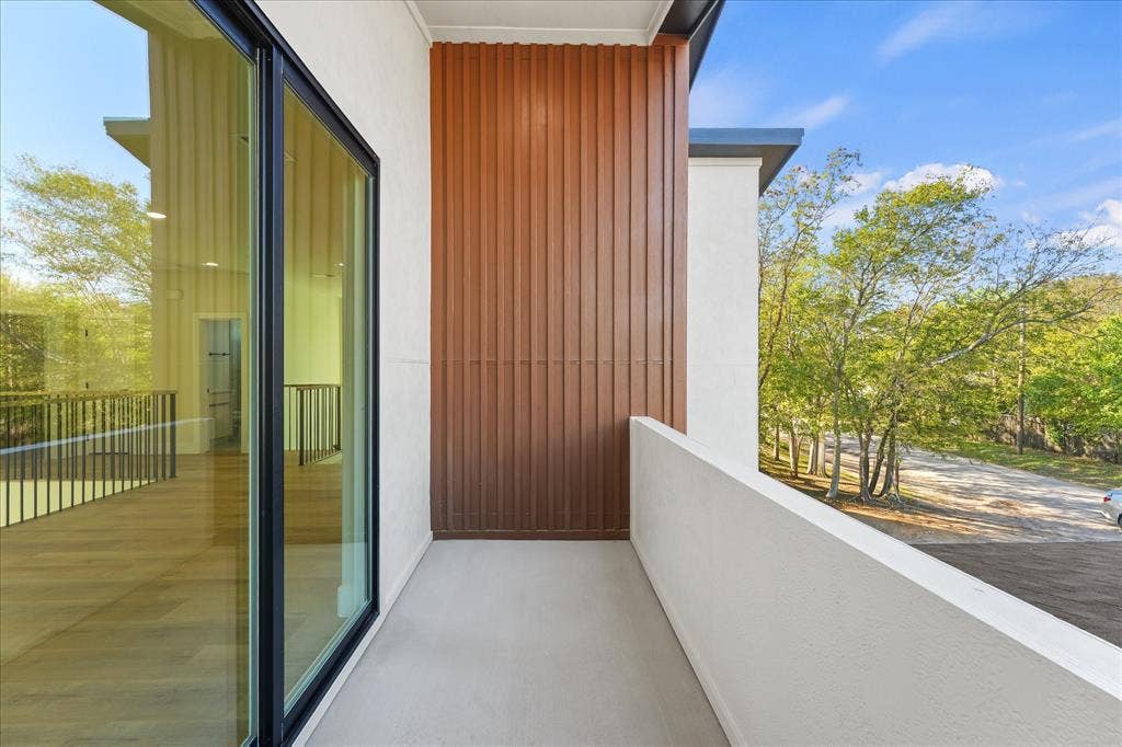 Exterior balcony featuring smooth stucco walls, corrugated metal accent paneling, and floor-to-ceiling glass sliding doors with black frames