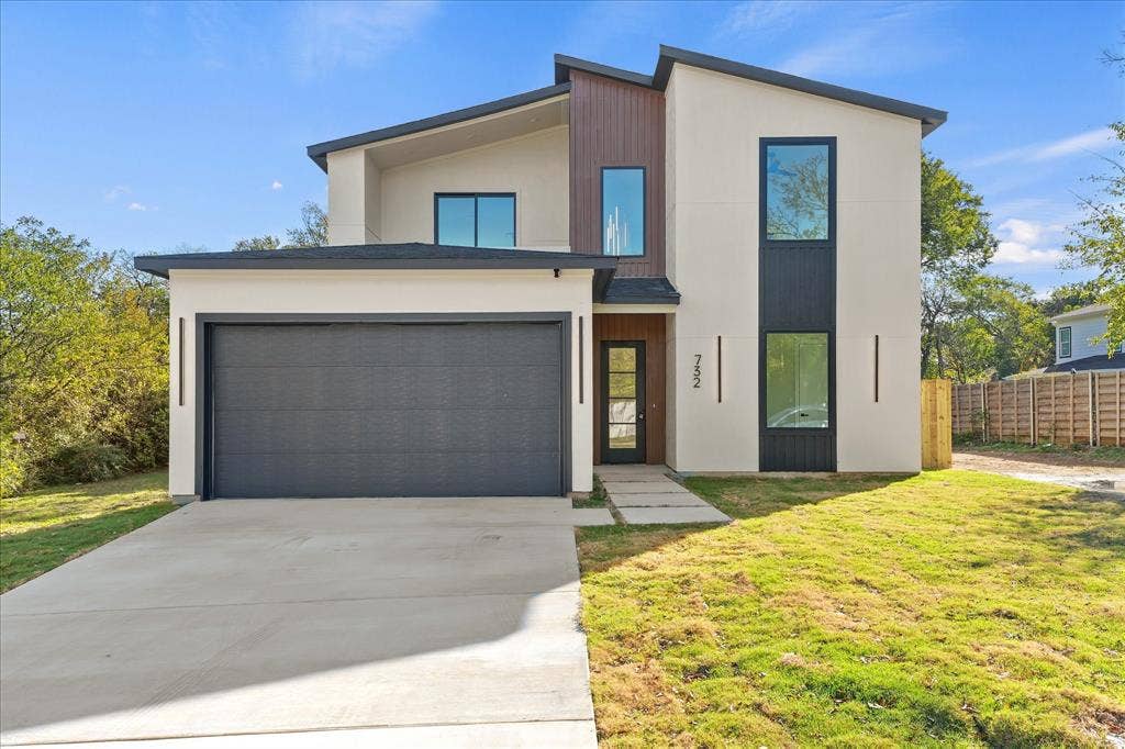 Modern two-story exterior featuring a mix of stucco and vertical wood-finish siding, a single-car garage, large rectangular windows with dark frames, and a concrete paver walkway