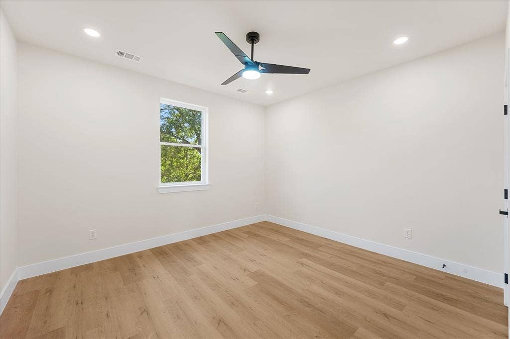 Neutral-toned room featuring wood-finish flooring, a matte black three-blade ceiling fan, recessed lighting, and a window with exterior greenery
