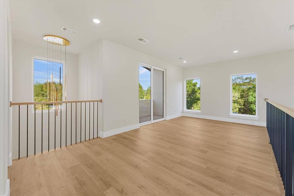 Open-concept space featuring wood-finish flooring, recessed lighting, expansive windows, a modern metal spindle railing, and sliding glass doors