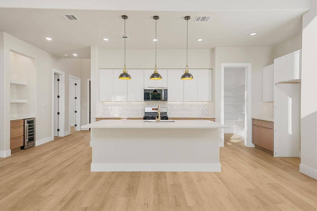 Kitchen featuring a central island with a quartz countertop, white flat-panel cabinetry, geometric pattern backsplash, three pendant lights, and built-in beverage refrigerator