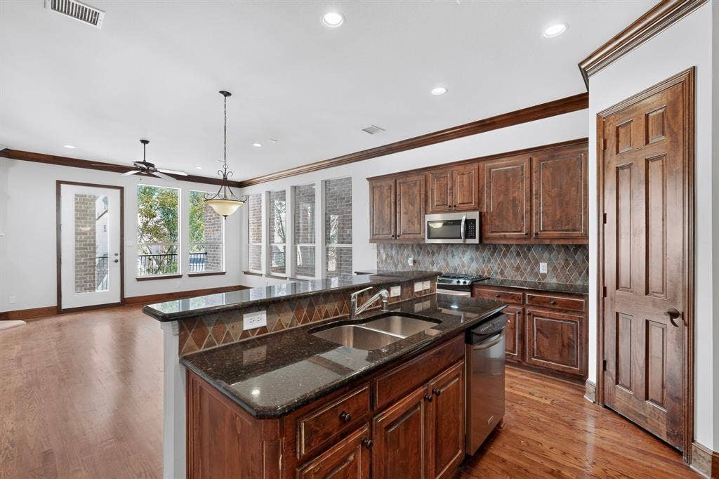 18359 Frankford Lakes Circle, Dallas, TX 75252 Kitchen featuring dark stone countertops, stained wood cabinetry, a tile backsplash, recessed lighting, and wood-finish flooring