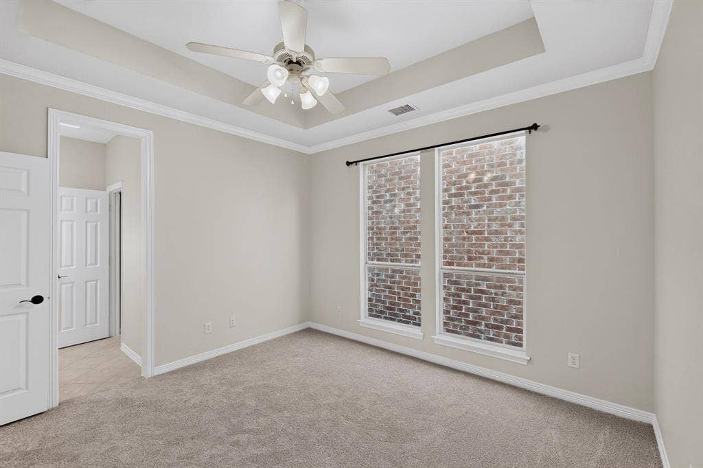 18359 Frankford Lakes Circle, Dallas, TX 75252 Tray ceiling with a central multi-light ceiling fan, wall-to-wall carpeting, and dual windows with brick exterior detailing