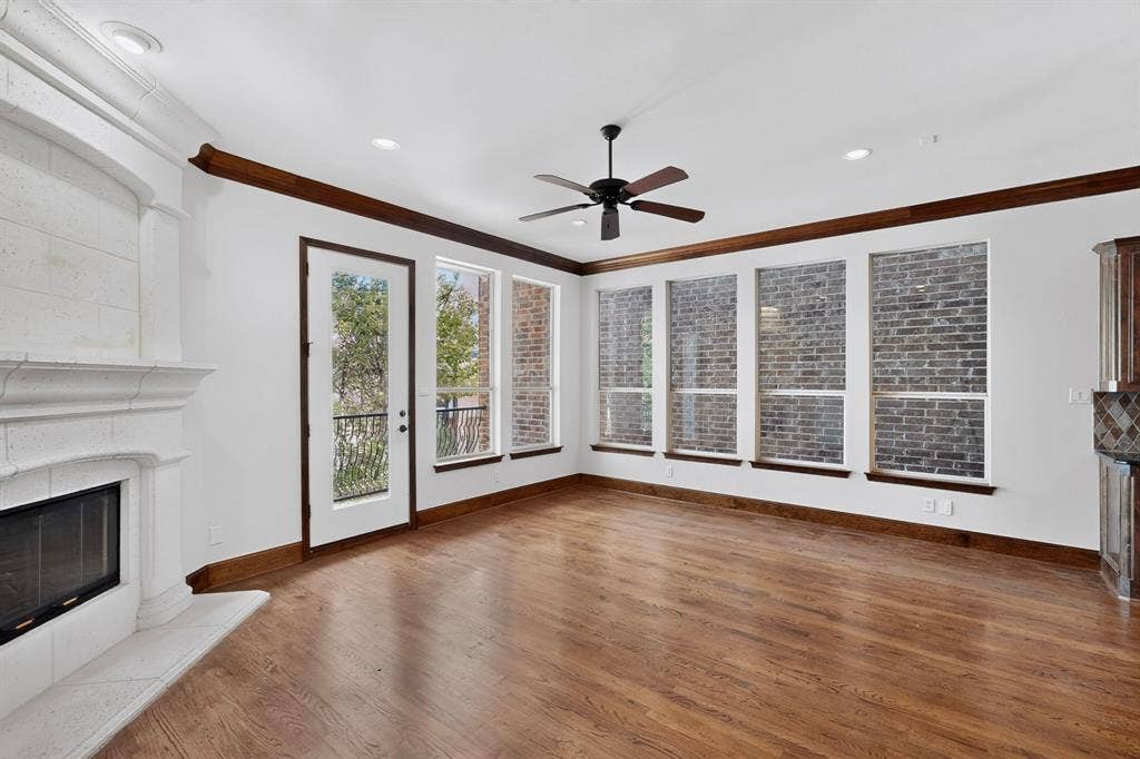 18359 Frankford Lakes Circle, Dallas, TX 75252 Living area featuring wood-finish flooring, a stone-surround fireplace, extensive brick wall accents, crown molding, and a ceiling fan