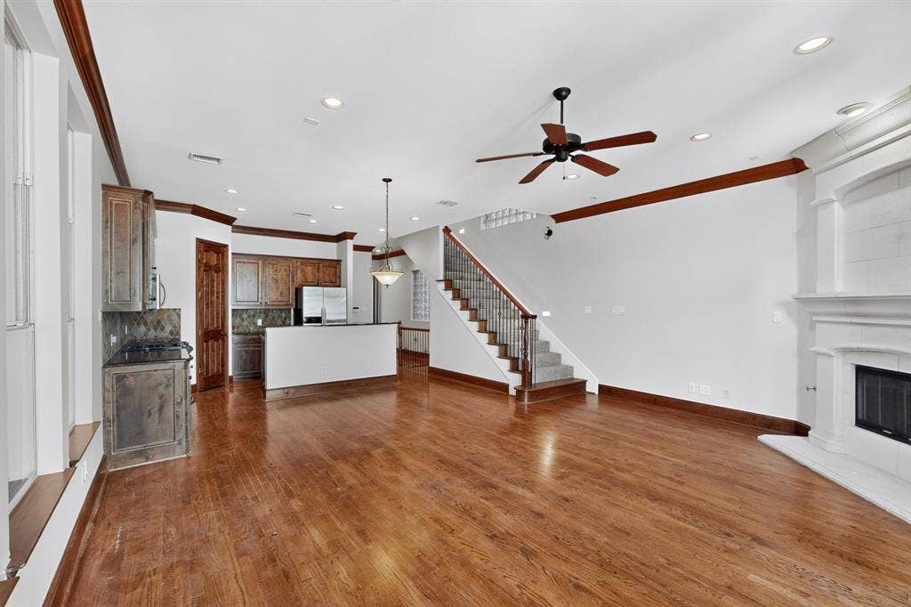18359 Frankford Lakes Circle, Dallas, TX 75252 Open-concept area featuring wood-finish flooring, a wood-burning fireplace with an ornate mantel, custom cabinetry, recessed lighting, and a staircase with a metal railing