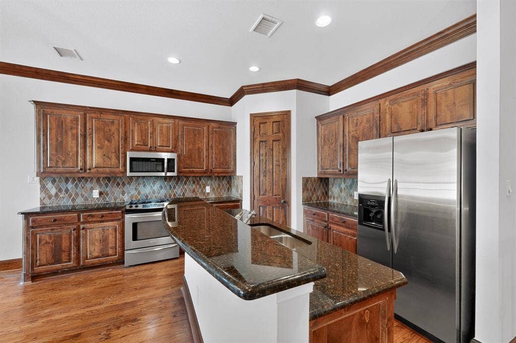 18359 Frankford Lakes Circle, Dallas, TX 75252 Kitchen featuring stained wood cabinetry, stone-finish countertops, diamond-pattern backsplash, stainless steel appliances, and wood-finish flooring