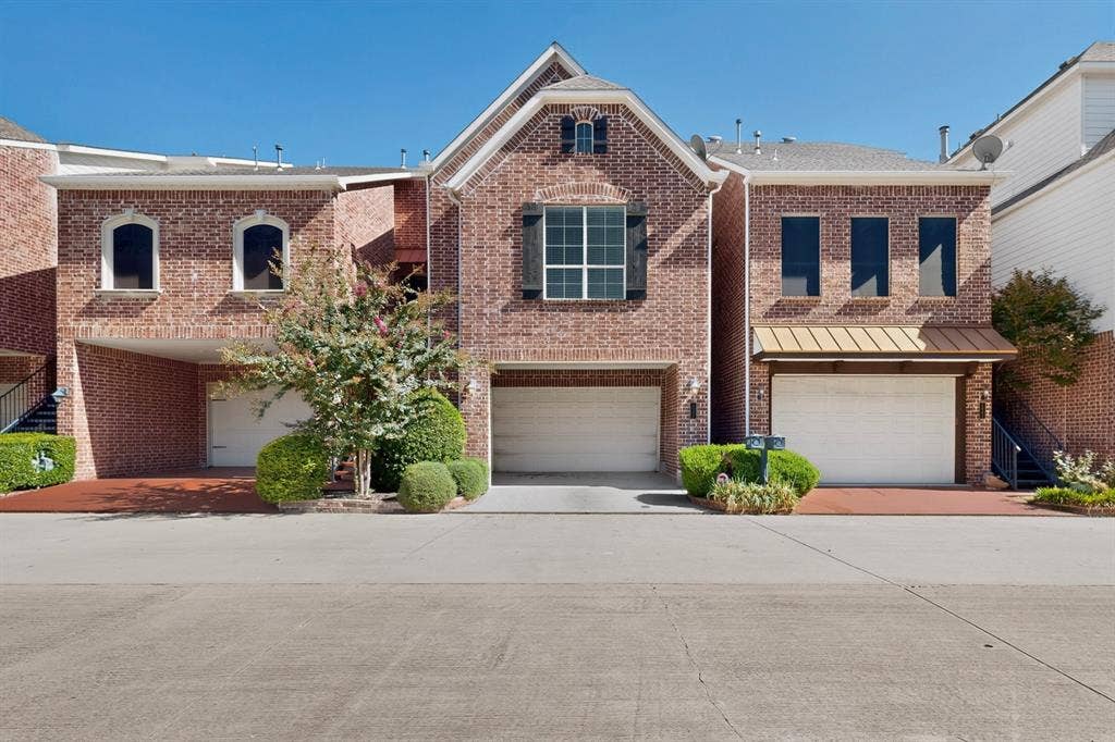18359 Frankford Lakes Circle, Dallas, TX 75252 Multi-level brick exterior featuring arched window detailing, three-car garage capacity, decorative shutters, and metal roof accents