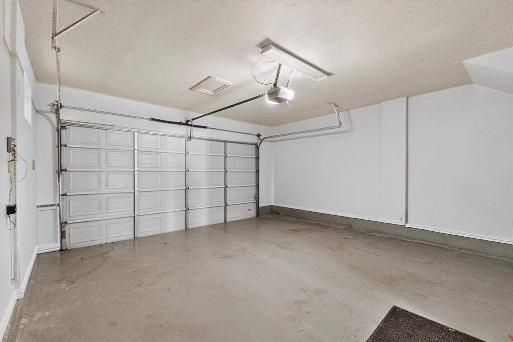 18359 Frankford Lakes Circle, Dallas, TX 75252 Attached garage featuring a multi-panel overhead door, automated garage door opener, finished walls, and concrete flooring