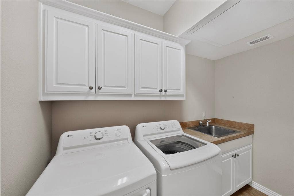 18359 Frankford Lakes Circle, Dallas, TX 75252 Laundry area featuring white shaker-style wall and base cabinetry, stone-finish countertops, and an integrated stainless steel basin sink