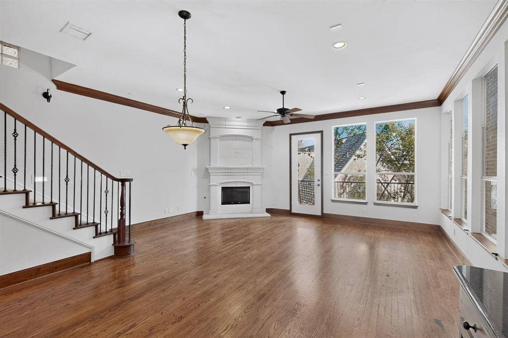 18359 Frankford Lakes Circle, Dallas, TX 75252 Wood-finish flooring, corner fireplace with a decorative mantel, staircase featuring a wrought-iron balustrade, crown molding, and large windows