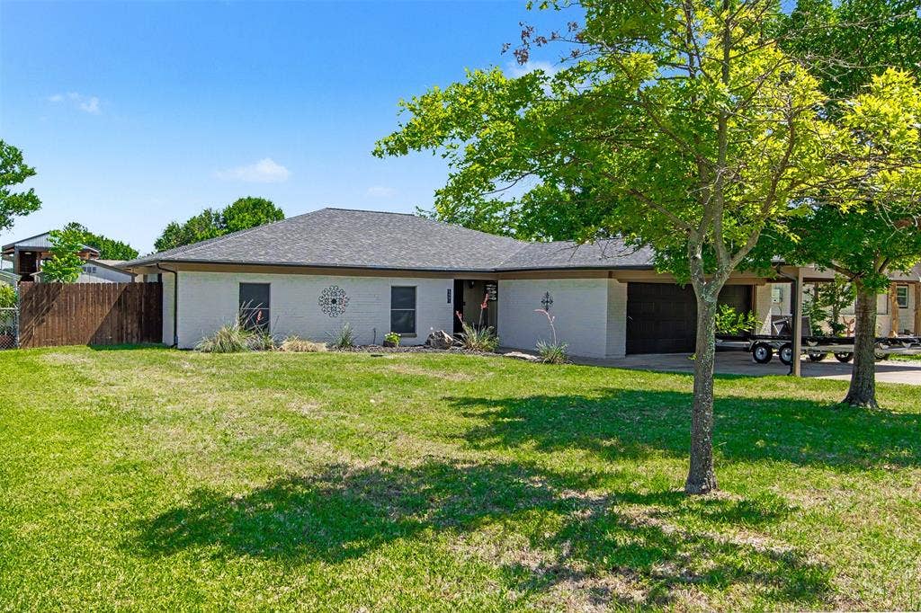 Single-story residence featuring a painted brick exterior, hip roof, multi-car garage, and expansive lawn with mature trees