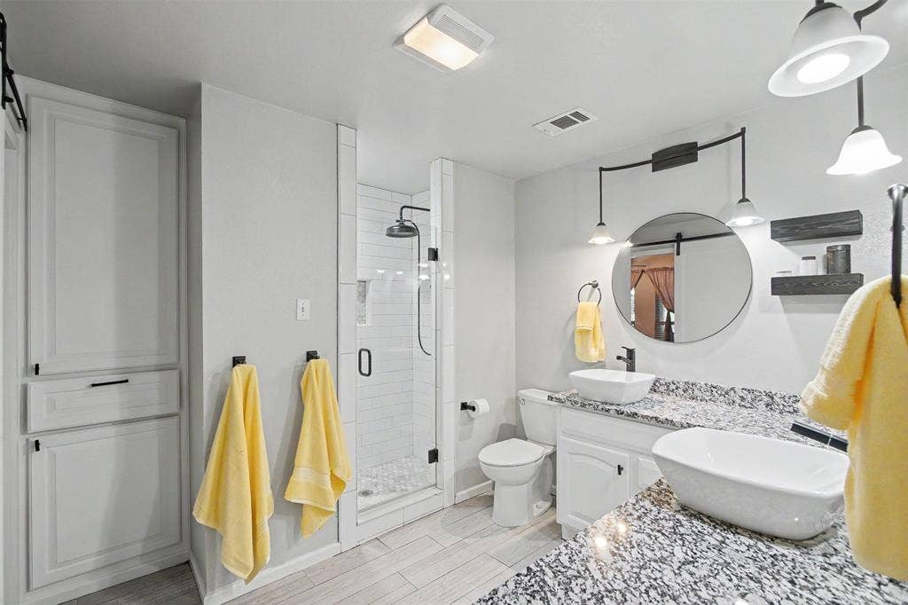 Bathroom featuring a double vanity with vessel sinks, speckled stone-finish countertops, a walk-in shower with white subway tile, and built-in floor-to-ceiling cabinetry