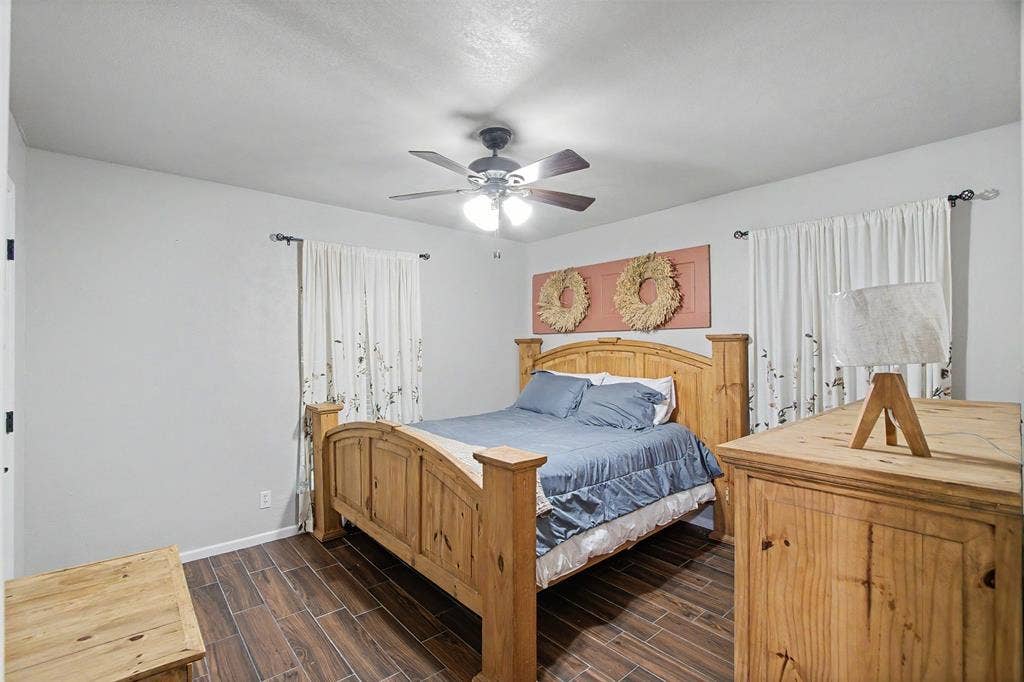 Room featuring wood-finish tile flooring, ceiling fan with integrated lighting, dual windows with wall-mounted curtain rods, and neutral interior paint