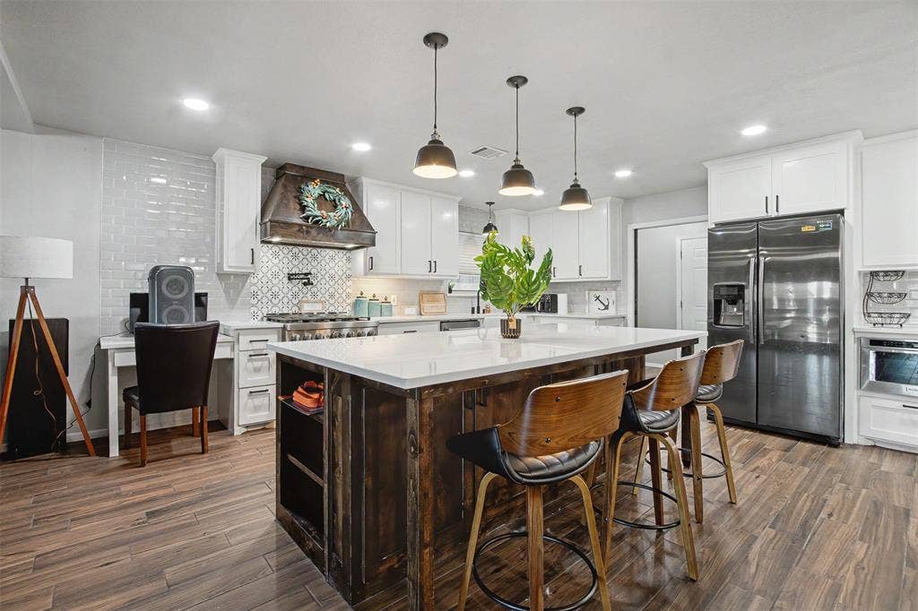 Kitchen featuring white shaker cabinetry, a center island with wood-tone base and light-colored countertop, subway tile backsplash, stainless steel appliances, and wood-finish flooring