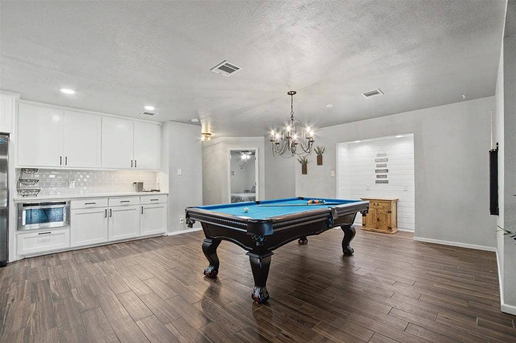 White shaker-style cabinetry with integrated microwave, wood-finish flooring, recessed lighting, and a multi-arm chandelier