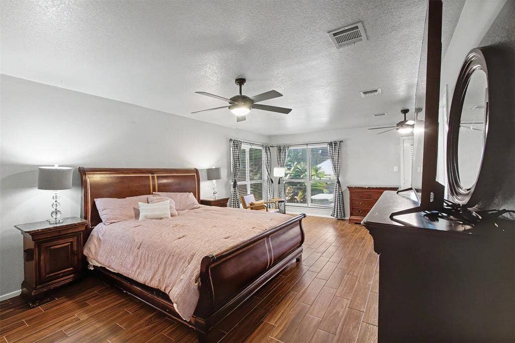 Spacious room featuring wood-finish flooring, dual ceiling fans with integrated lighting, and multiple windows