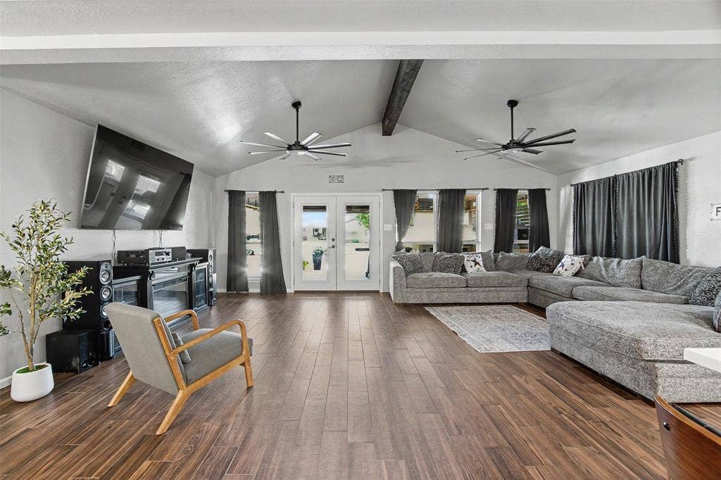Vaulted ceilings with exposed decorative beam, wood-finish flooring, dual multi-blade ceiling fans, and glass-paneled double doors