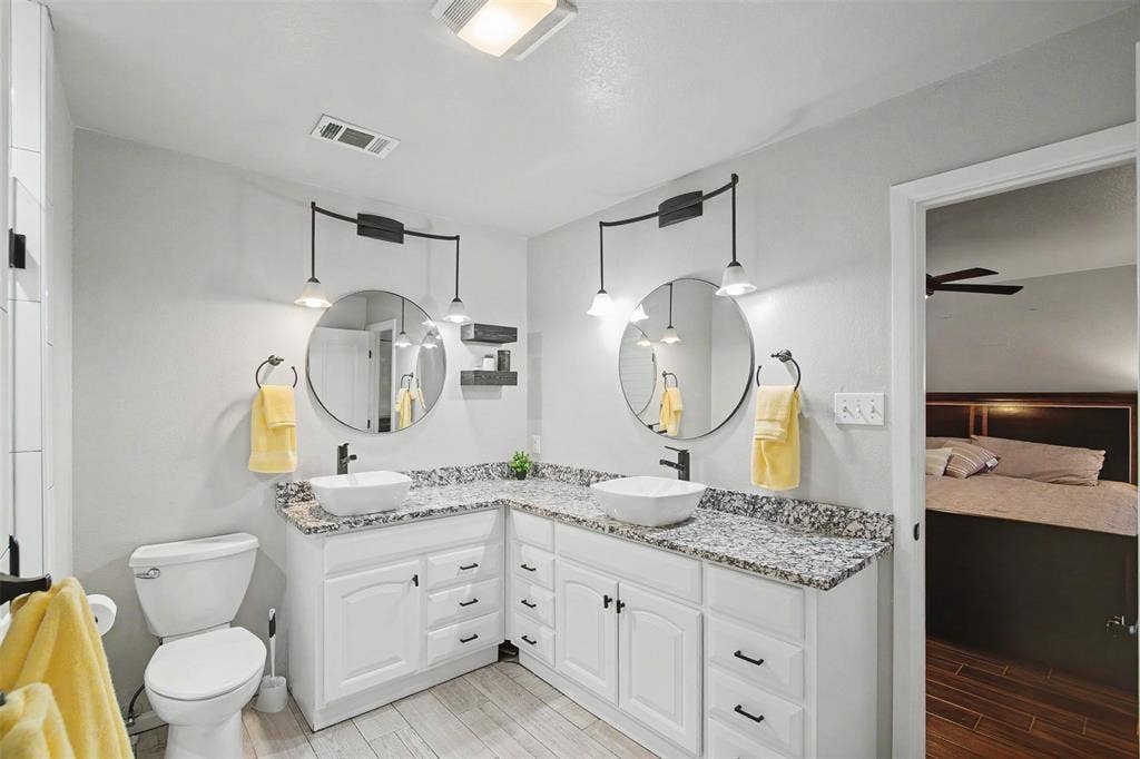 Dual vanity featuring white cabinetry, stone-patterned countertops, two round mirrors, and black-finish hardware