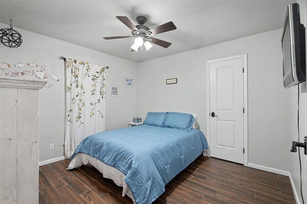 Interior space featuring wood-finish flooring, a multi-blade ceiling fan with integrated lighting, and a solid-core interior door with a matte black lever handle
