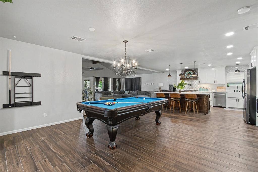 Open-concept area featuring wood-finish flooring, recessed lighting, a decorative chandelier, and a kitchen equipped with white cabinetry, a center island with a wood base, and a farmhouse-style sink