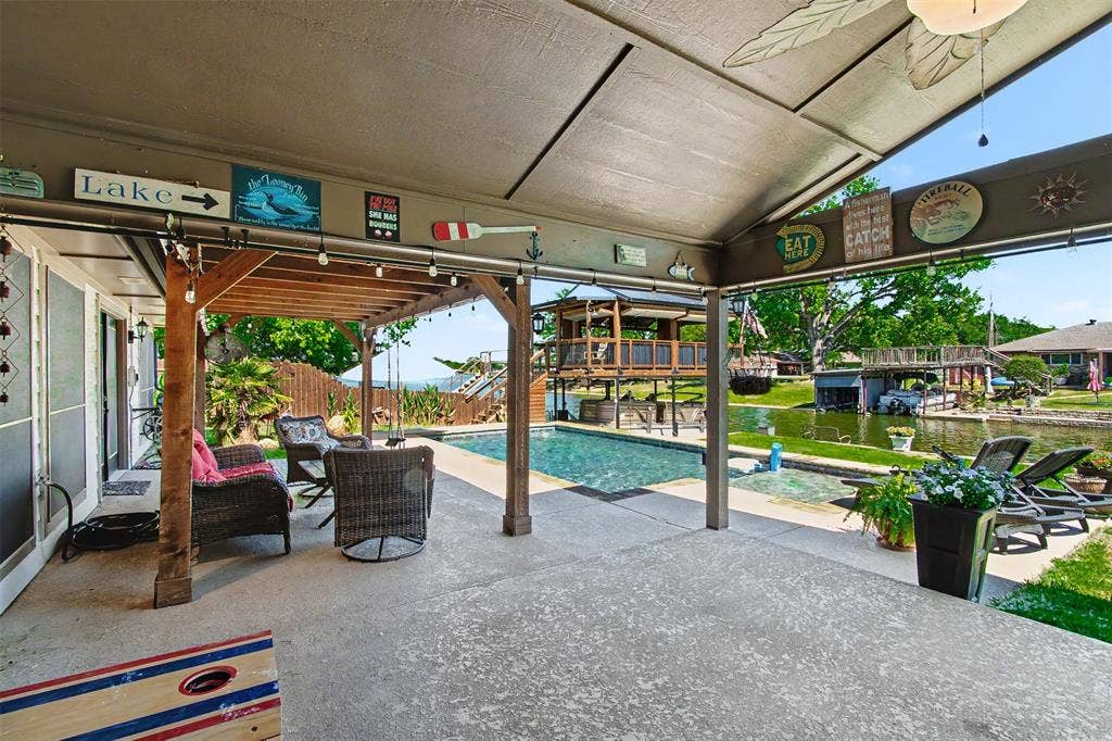 Covered patio with wood-post support beams, concrete flooring, and an inground swimming pool situated on the water's edge