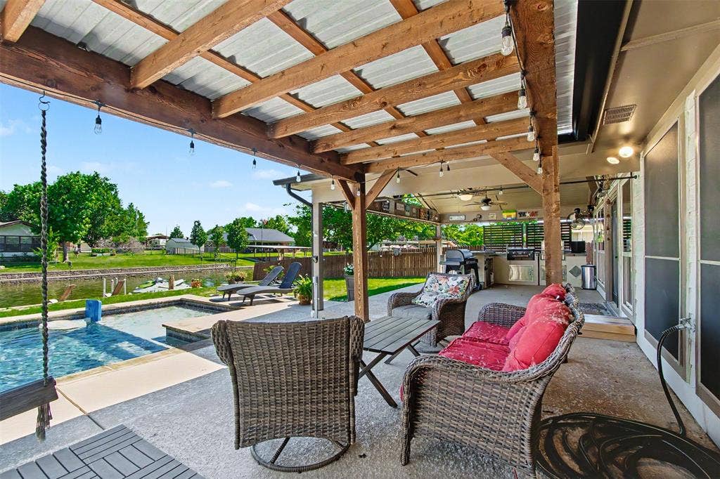 Covered patio featuring a timber-frame pergola, built-in outdoor kitchen, concrete decking, and an inground pool