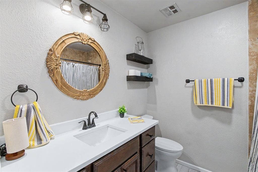 Bathroom featuring a vanity with white countertop, dark wood-finish cabinetry, matte black hardware, and a circular decorative mirror with ornate detailing