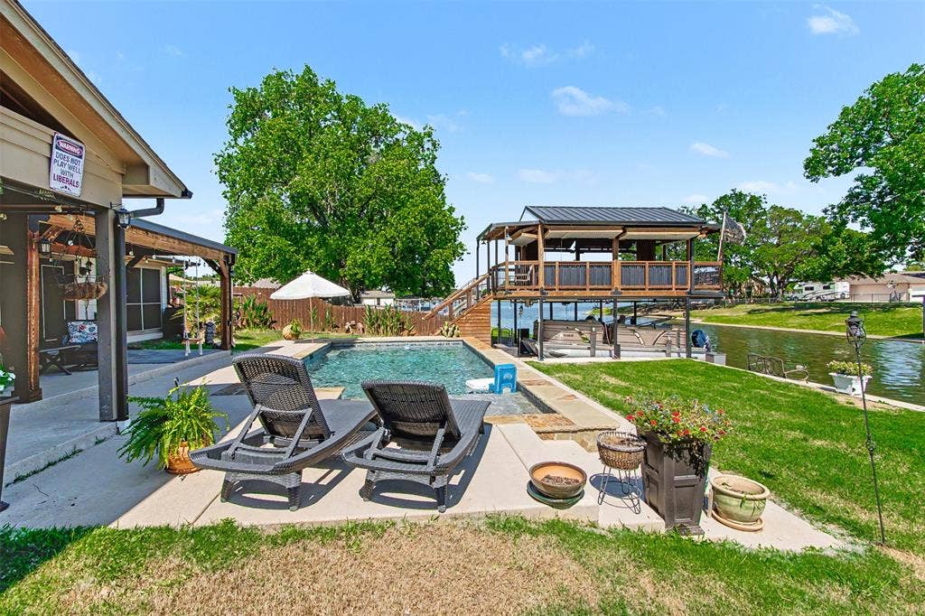 In-ground swimming pool with stone coping, concrete patio, waterfront deck with overhead structure, and bulkhead