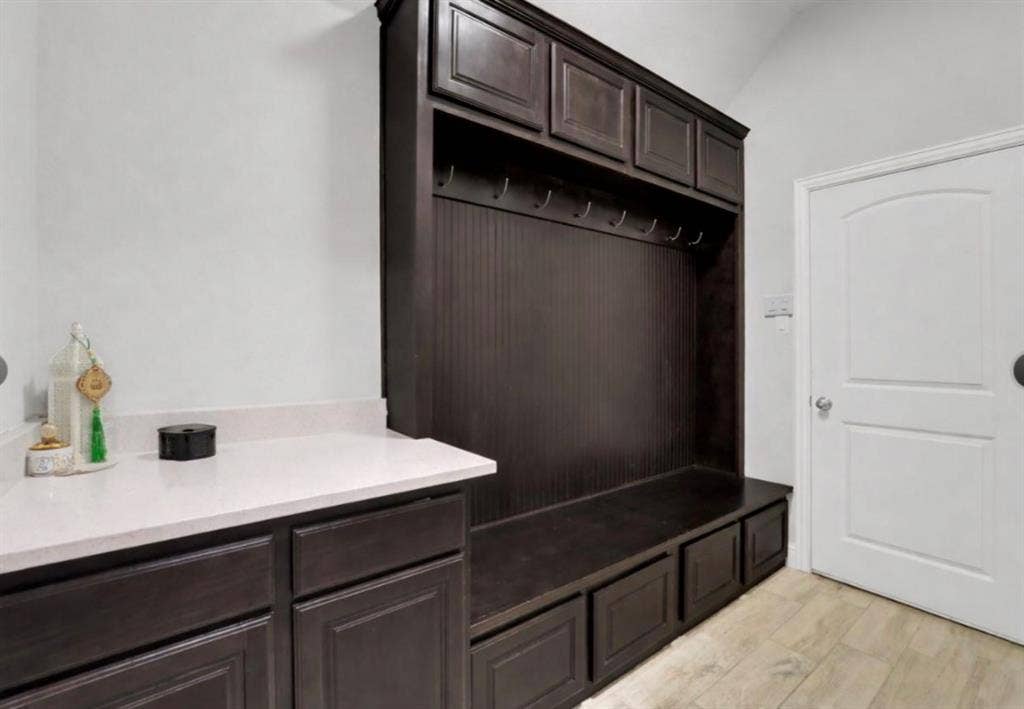 102 Champion Drive, Wylie, TX 75098 Built-in dark wood cabinetry featuring integrated storage bench, beadboard detailing, and overhead lockers, complemented by a stone-surface countertop and wood-finish flooring