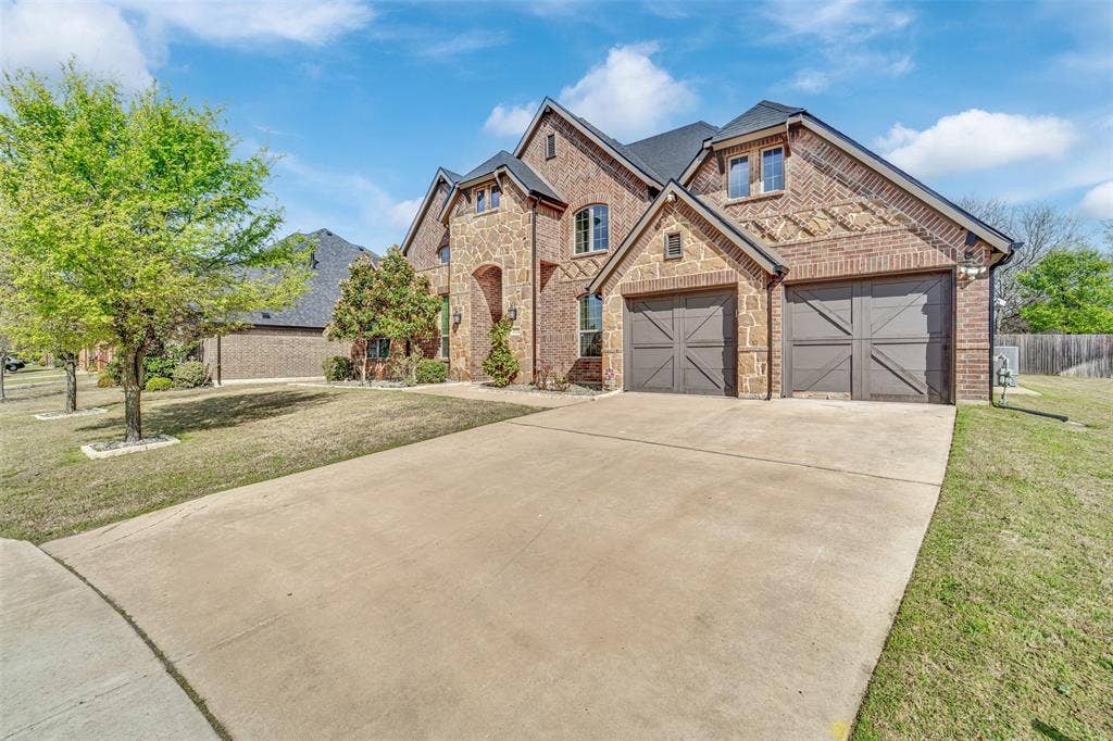 102 Champion Drive, Wylie, TX 75098 Brick exterior featuring multi-gabled rooflines, decorative masonry detailing, and attached two-car garage with cross-buck carriage doors
