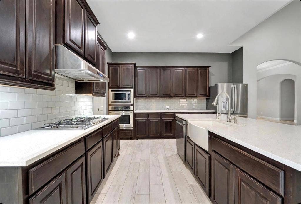 102 Champion Drive, Wylie, TX 75098 Kitchen featuring dark-finish cabinetry, stone-surface countertops, white subway tile backsplash, farmhouse sink, and wood-finish tile flooring