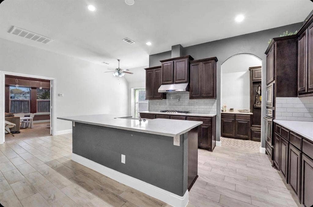 102 Champion Drive, Wylie, TX 75098 Kitchen featuring a central island with quartz countertops, custom wood cabinetry, a subway tile backsplash, built-in stainless steel oven, and wood-finish tile flooring