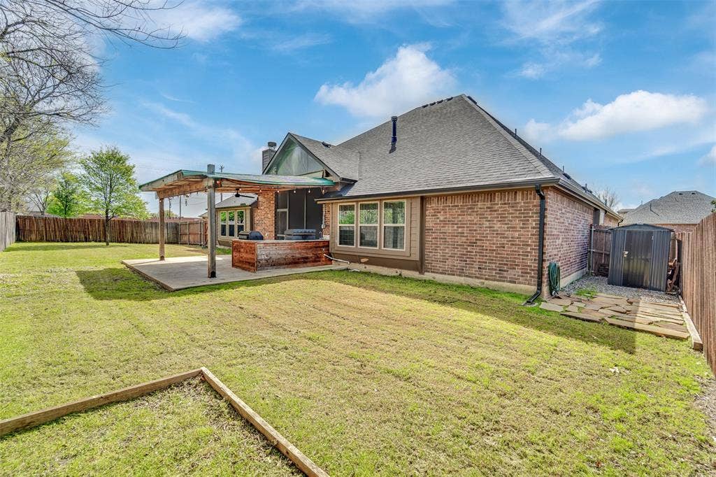 102 Champion Drive, Wylie, TX 75098 Rear exterior featuring a brick facade, covered wood-beam patio, concrete slab, and wood privacy fencing