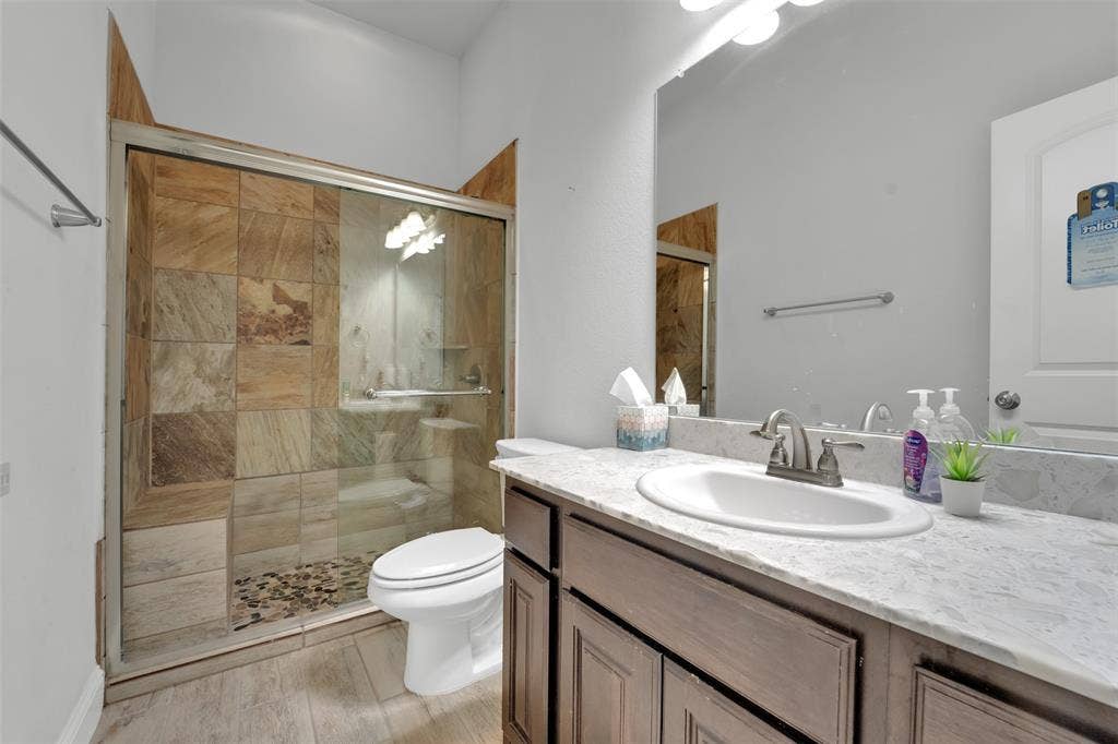 102 Champion Drive, Wylie, TX 75098 Bathroom featuring a vanity with a light-toned stone countertop, an integrated oval sink, and dark wood-finish cabinetry