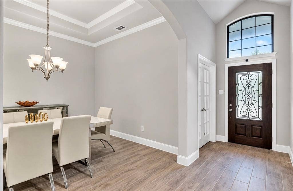 102 Champion Drive, Wylie, TX 75098 Entryway featuring a wood-finish entry door with decorative iron inlay, arched transom window, wood-finish flooring, tray ceiling, and multi-arm chandelier