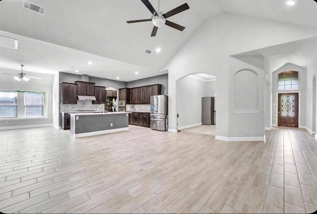 102 Champion Drive, Wylie, TX 75098 Open-concept interior featuring vaulted ceilings, wood-finish flooring, dark cabinetry, recessed lighting, and an arched entryway with decorative transom window