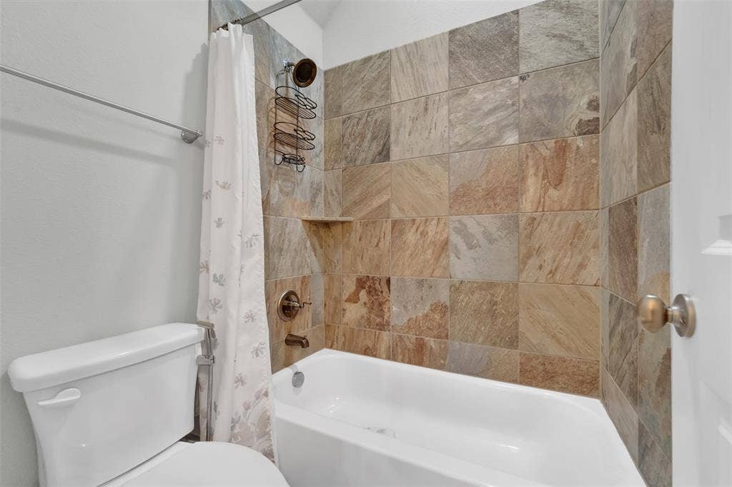 102 Champion Drive, Wylie, TX 75098 Full-size bathtub with multi-toned stone tile surround, integrated shelving, and bronze-finish plumbing fixtures
