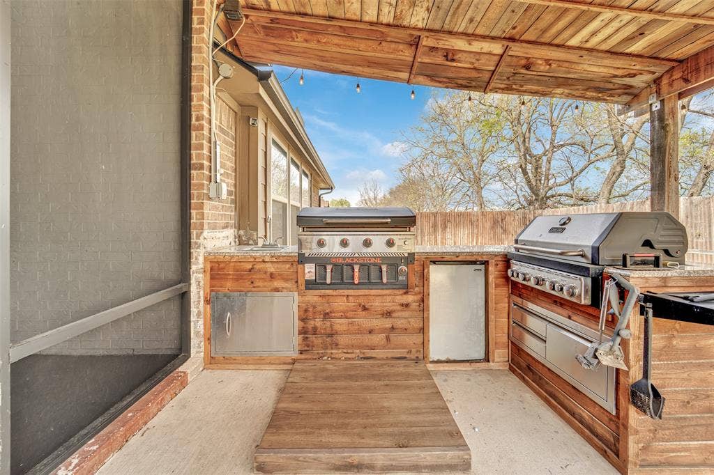 102 Champion Drive, Wylie, TX 75098 Covered outdoor kitchen featuring wood-paneled cabinetry, stone countertops, stainless steel appliances, and a wood-slat ceiling