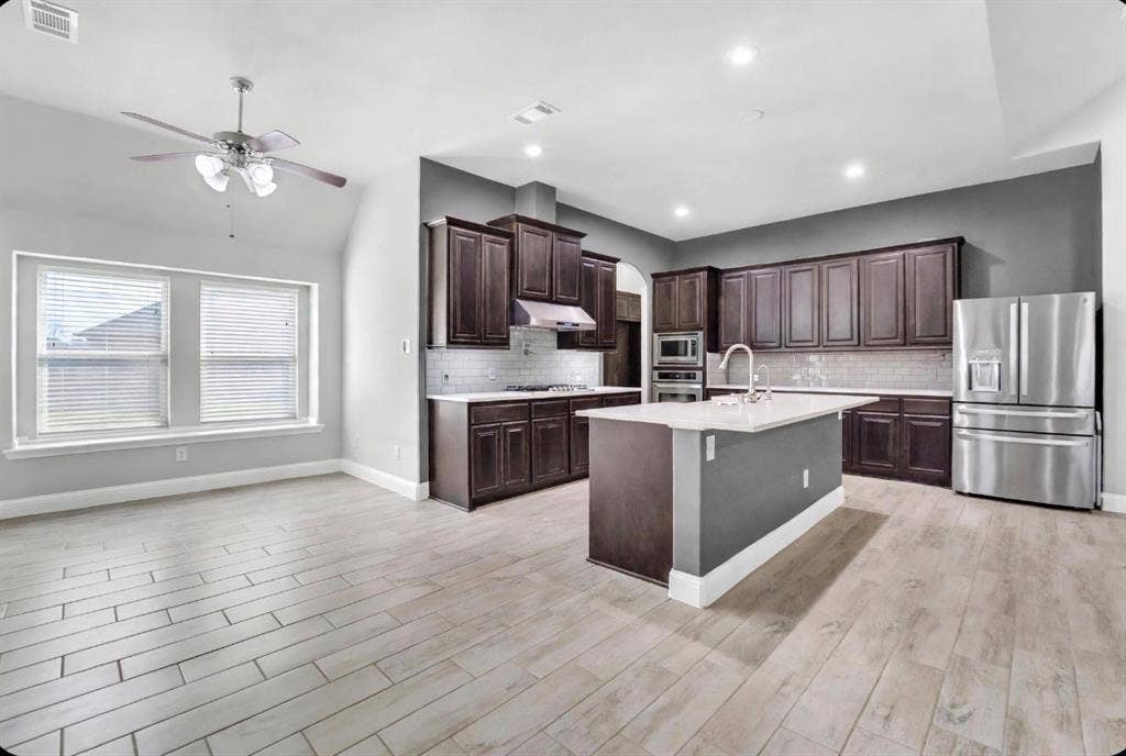 102 Champion Drive, Wylie, TX 75098 Kitchen featuring dark wood cabinetry, a central island with a stone countertop, stainless steel appliances, subway tile backsplash, and wood-finish tile flooring