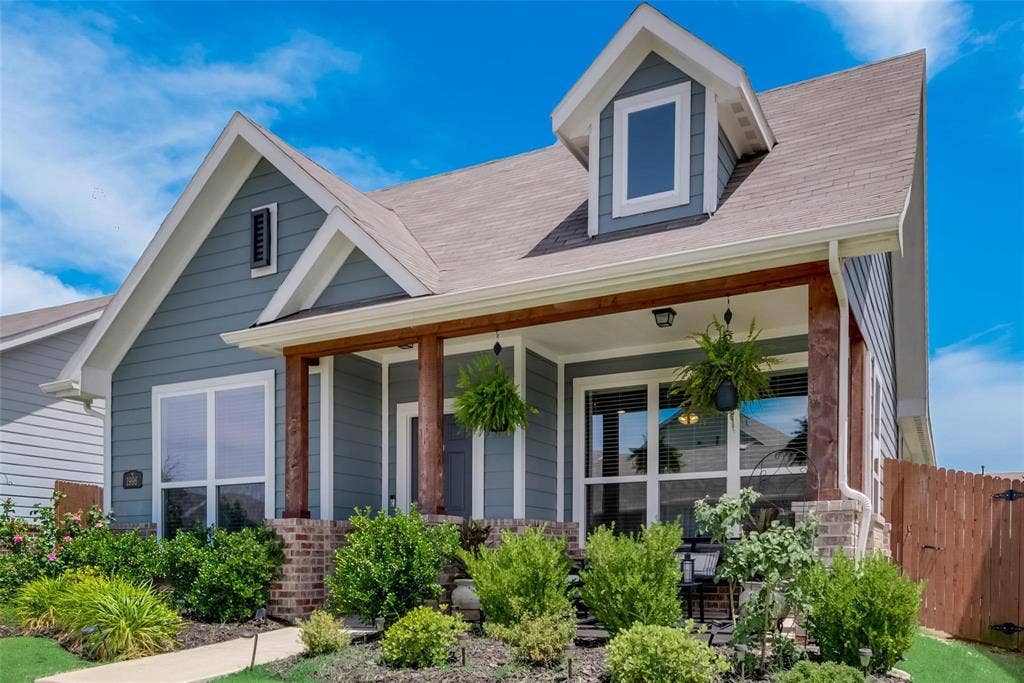 1996 Sunnybrook Drive, Heartland, TX 75126 Exterior featuring gray horizontal siding, a covered front porch with stained wood columns, stone masonry pier bases, and a front-facing dormer window
