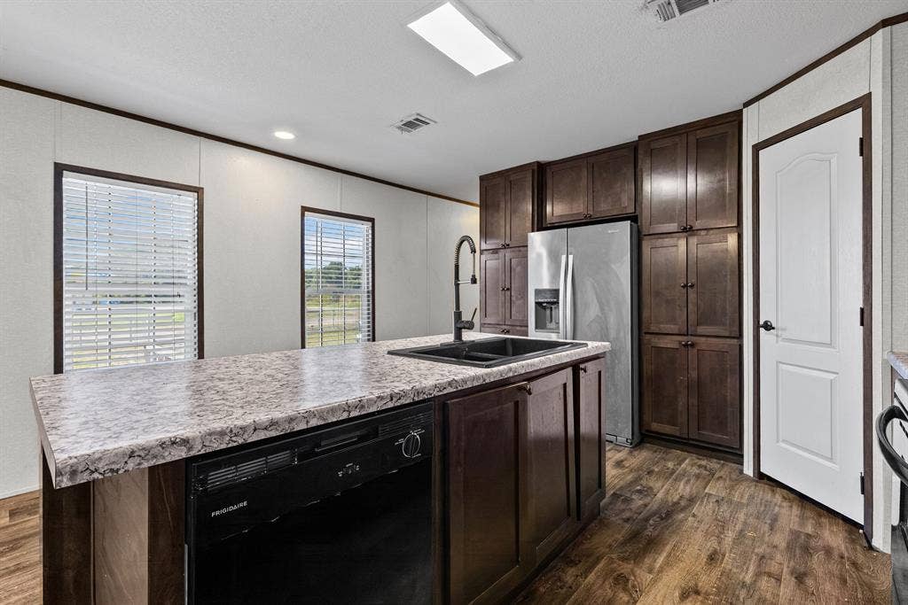 Kitchen featuring dark wood-finish cabinetry, patterned laminate countertops, a center island with a drop-in sink, matte black hardware, and wood-finish flooring