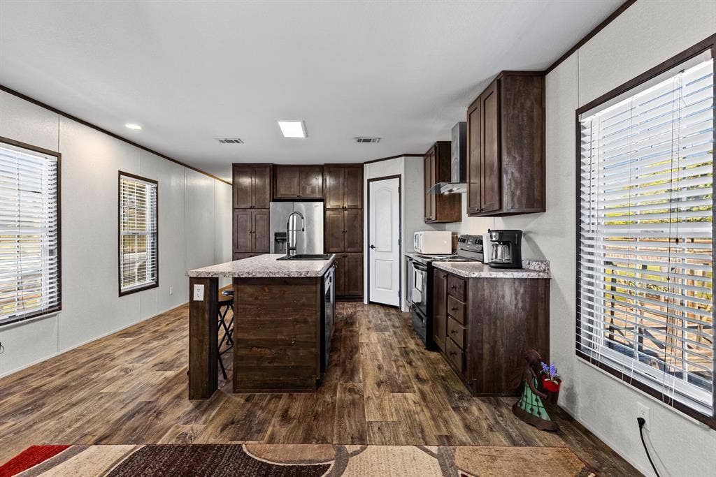 Kitchen featuring dark wood-finish cabinetry, a central island with a stone-finish countertop, stainless steel appliances, and wood-finish flooring